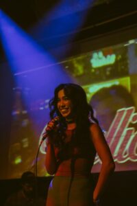 The singer Wallice on stage holding a microphone with her name projected onto the backdrop.